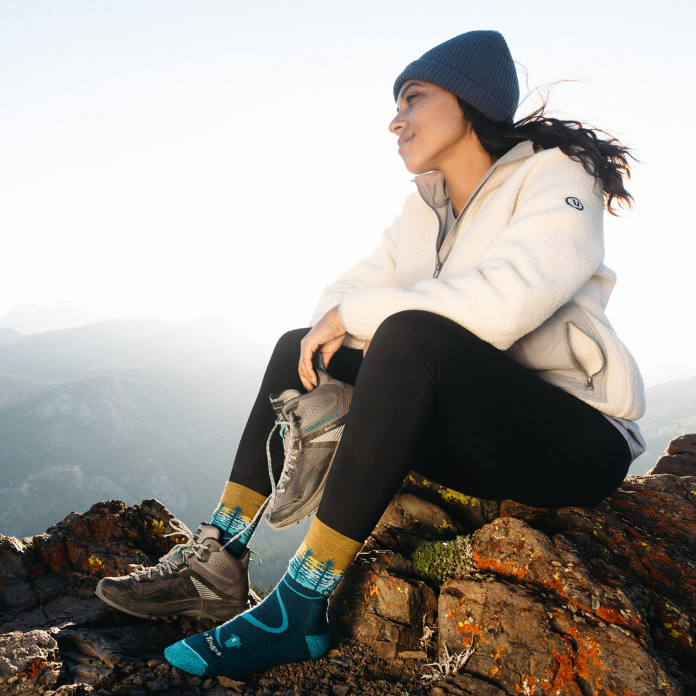Women's northwoods socks worn by a seated hiker on a mountain summit, full scene
