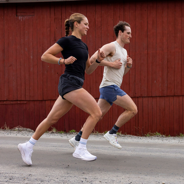 Two runners passing a red barn, one wearing men&