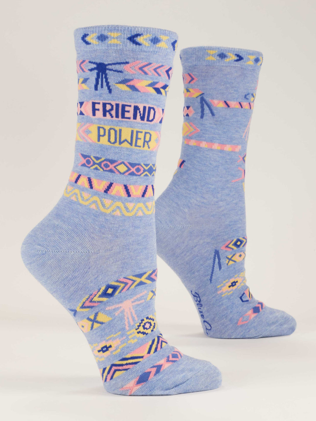 The Blue Q Friend Power W-Crew Socks feature light blue combed cotton, colorful geometric arrows and zigzags in pastel yellow, pink, and blue, plus "FRIEND POWER" in bold letters. Sustainable design.