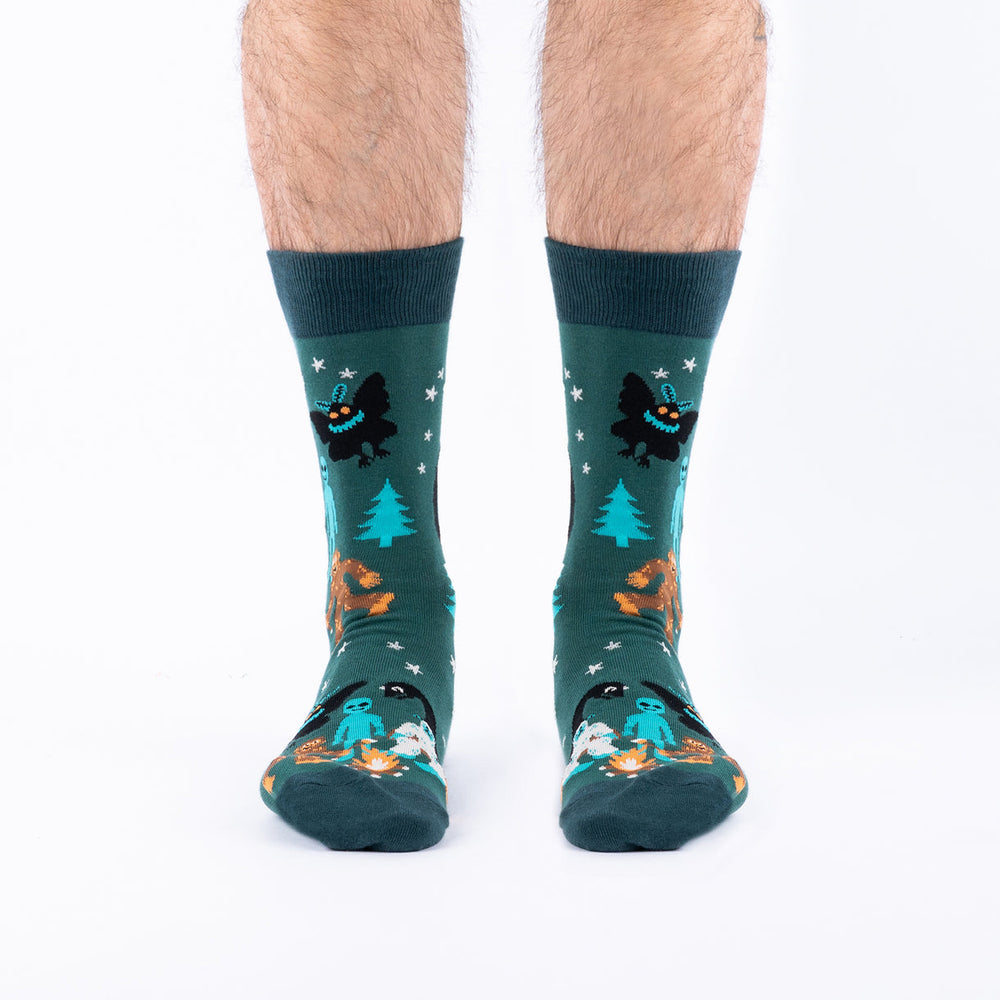 Men's cryptid crew socks worn, front view with Mothman and pine trees