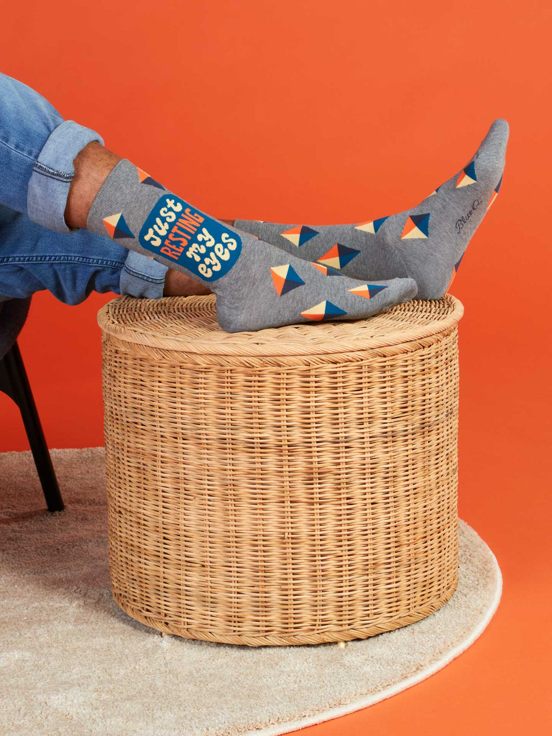 A person lounges with feet up on a round wicker table, wearing Blue Q&