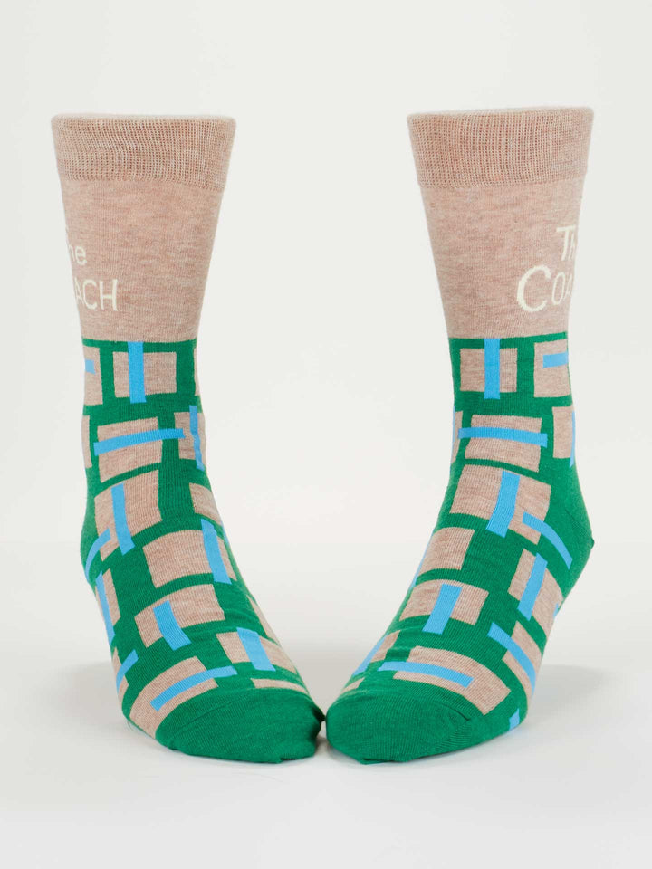 The Coach M-Crew Socks by Blue Q feature beige cuffs, green feet, and a blue, beige, and tan geometric rectangle pattern. "The Coach" is stitched in white on the cuffs. Made from combed cotton; fits men’s shoe sizes comfortably.