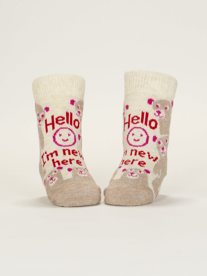 A pair of beige Blue Q baby socks featuring pink and brown animal faces, a smiling sun, and "Hello I&