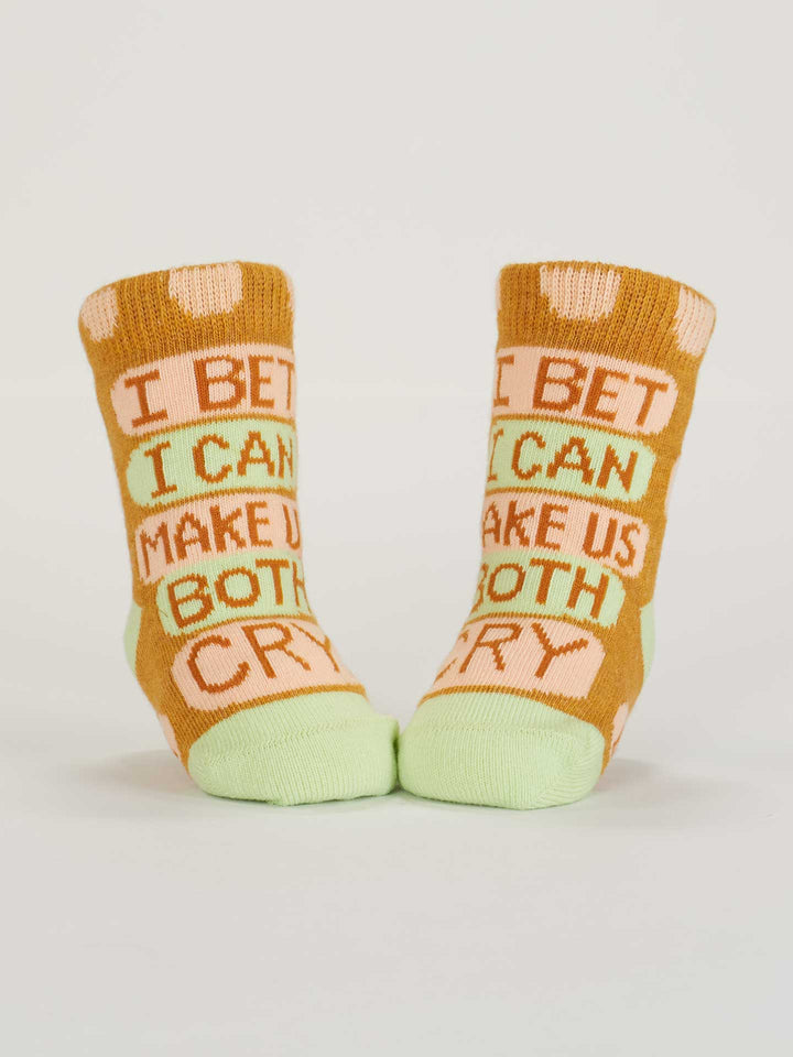 Blue Q’s Certified Cuddle Bug/I Bet I Can Make Us Both Cry Baby Socks are soft organic cotton pairs in orange, green, and pink with playful slogans. OCS Certified for quality—perfect for your little one’s feet.