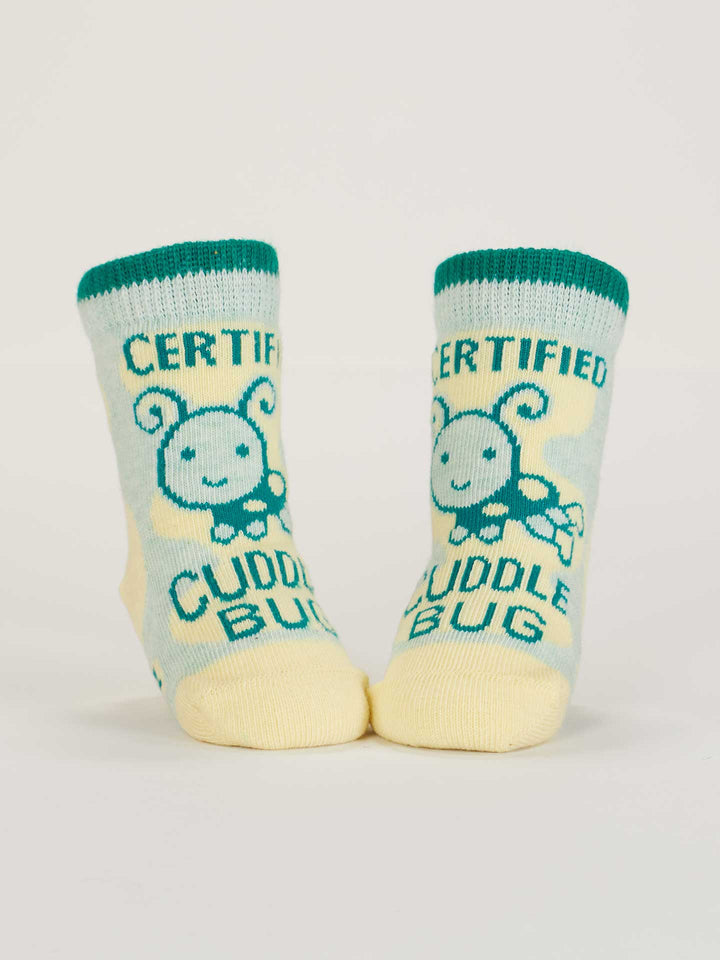 Blue Q Certified Cuddle Bug/I Bet I Can Make Us Both Cry baby socks: light blue and yellow, green cuffs, adorable bug design with "Certified Cuddle Bug" on each sock, crafted from soft organic cotton.