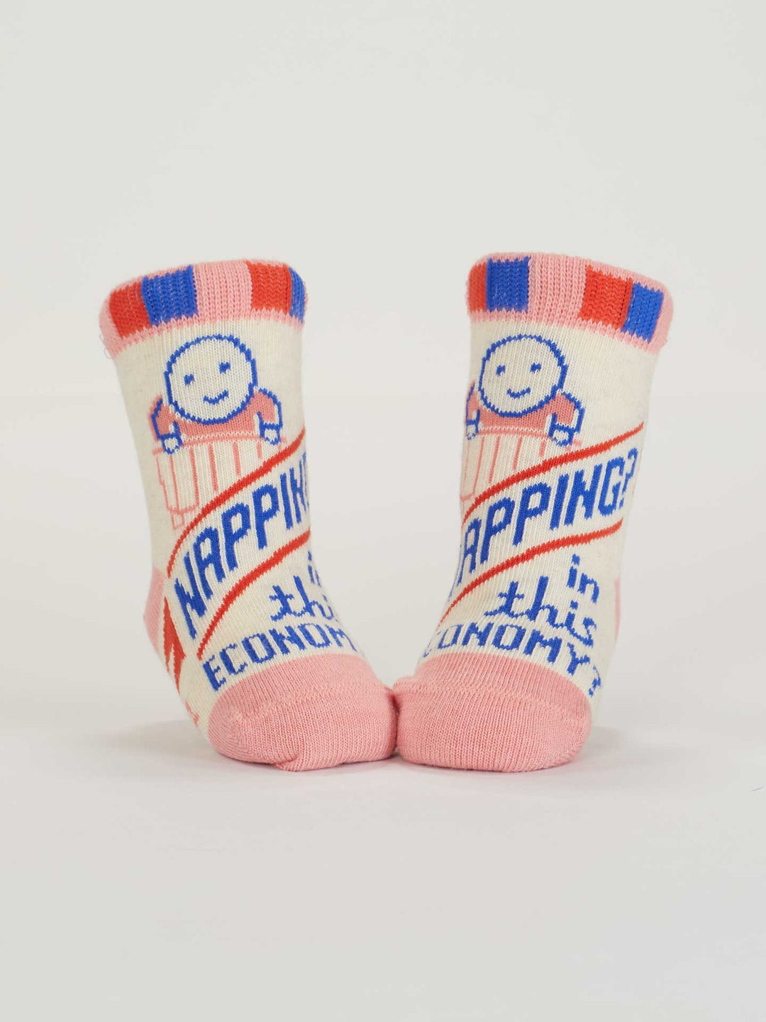 Blue Q’s Napping? In This Economy?/Poop Machine Baby Socks are OCS Certified Organic Cotton with pink toes and cuffs, red and blue stripes, smiling faces, and “NAPPING? in this ECONOMY?” text—perfect for nap time comfort.