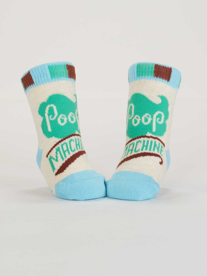 A pair of Blue Q Napping? In This Economy?/Poop Machine baby socks in cream, brown, and light blue organic cotton, with "Poop Machine" text and a green cartoon poop graphic, shown upright on a white background.