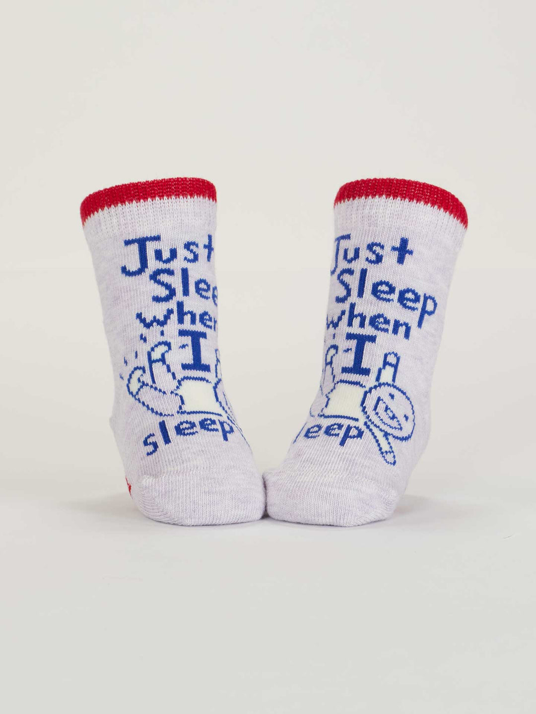 A pair of OCS certified organic cotton Blue Q baby socks, red cuffs, blue "Just Sleep When I Sleep. Lol." text and a sleeping baby drawing on the front. Product name: Wait &