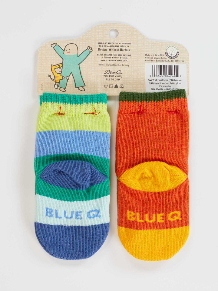 Blue Q "One Tough Customer/Reflecting On My Behavior" baby socks set: two pairs of colorful organic cotton socks (blue/green with "BLUE" text, and orange/yellow) on a hanger featuring a cat and waving person. Ideal newborn gift.