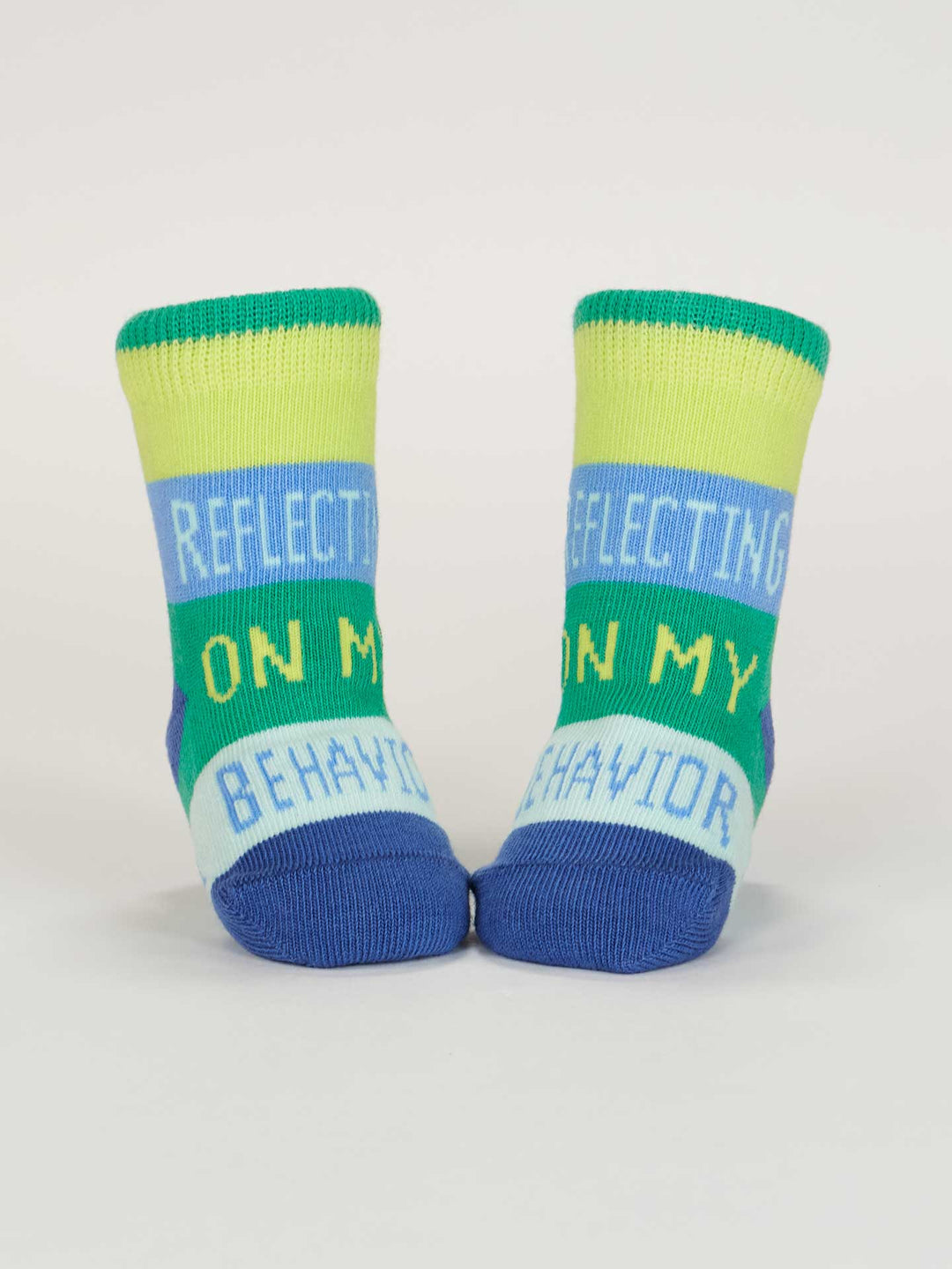 Blue Q’s One Tough Customer/ Reflecting On My Behavior Baby Socks feature green, blue, and yellow stripes with “REFLECTING ON MY BEHAVIOR” in white and yellow letters. Made from organic cotton for babies 0-12 months.