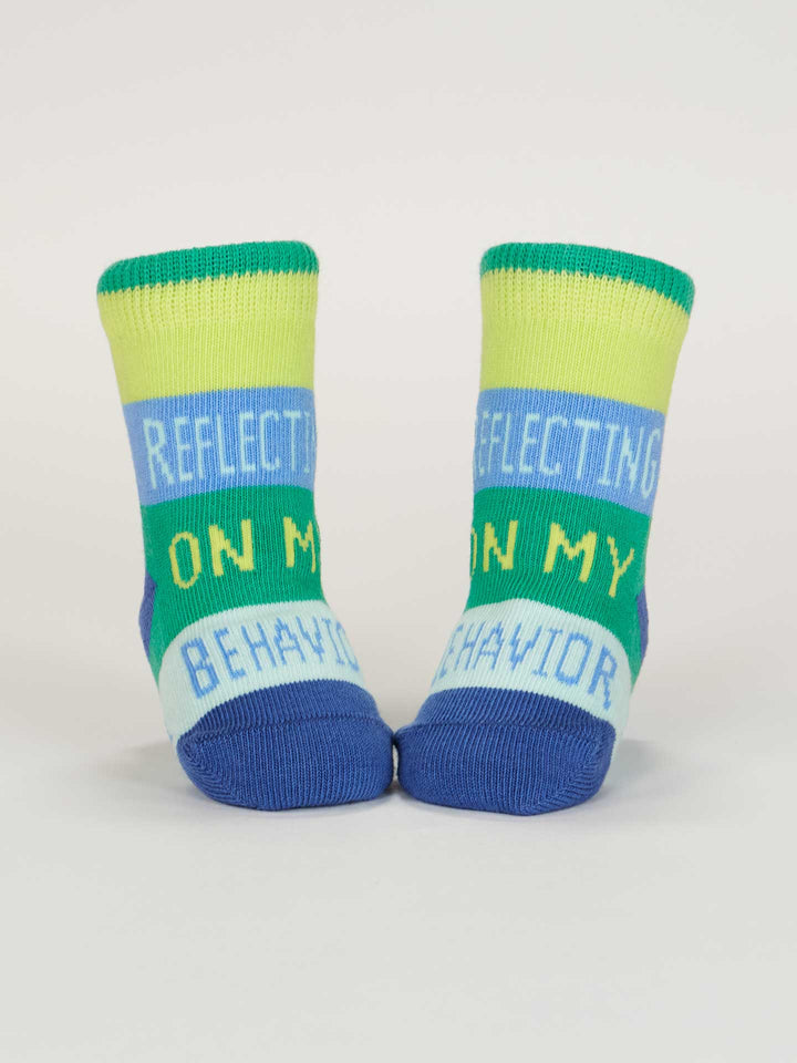 Blue Q’s One Tough Customer/ Reflecting On My Behavior Baby Socks feature green, blue, and yellow stripes with “REFLECTING ON MY BEHAVIOR” in white and yellow letters. Made from organic cotton for babies 0-12 months.