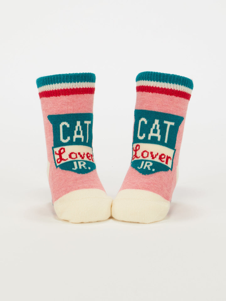 Blue Q’s Cat Lover Jr./The Baby Did It. Baby Socks are pink and cream organic cotton, accented in teal, red, and white, with "CAT Lover JR." on the front—perfect for little cat fans!.