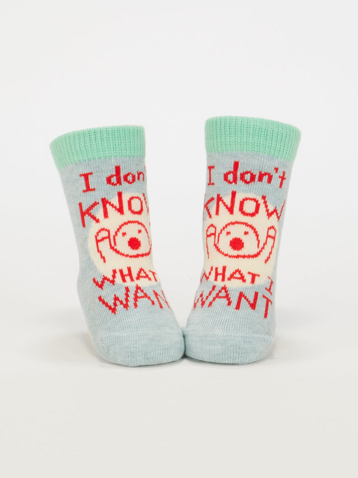 Blue Q’s “I Don’t Know What I Want/Binky! Binky! Binky!” baby socks are light blue organic cotton with mint cuffs, a red cartoon face, and “I don’t know what I want” text. Fits babies aged 0-12 months.