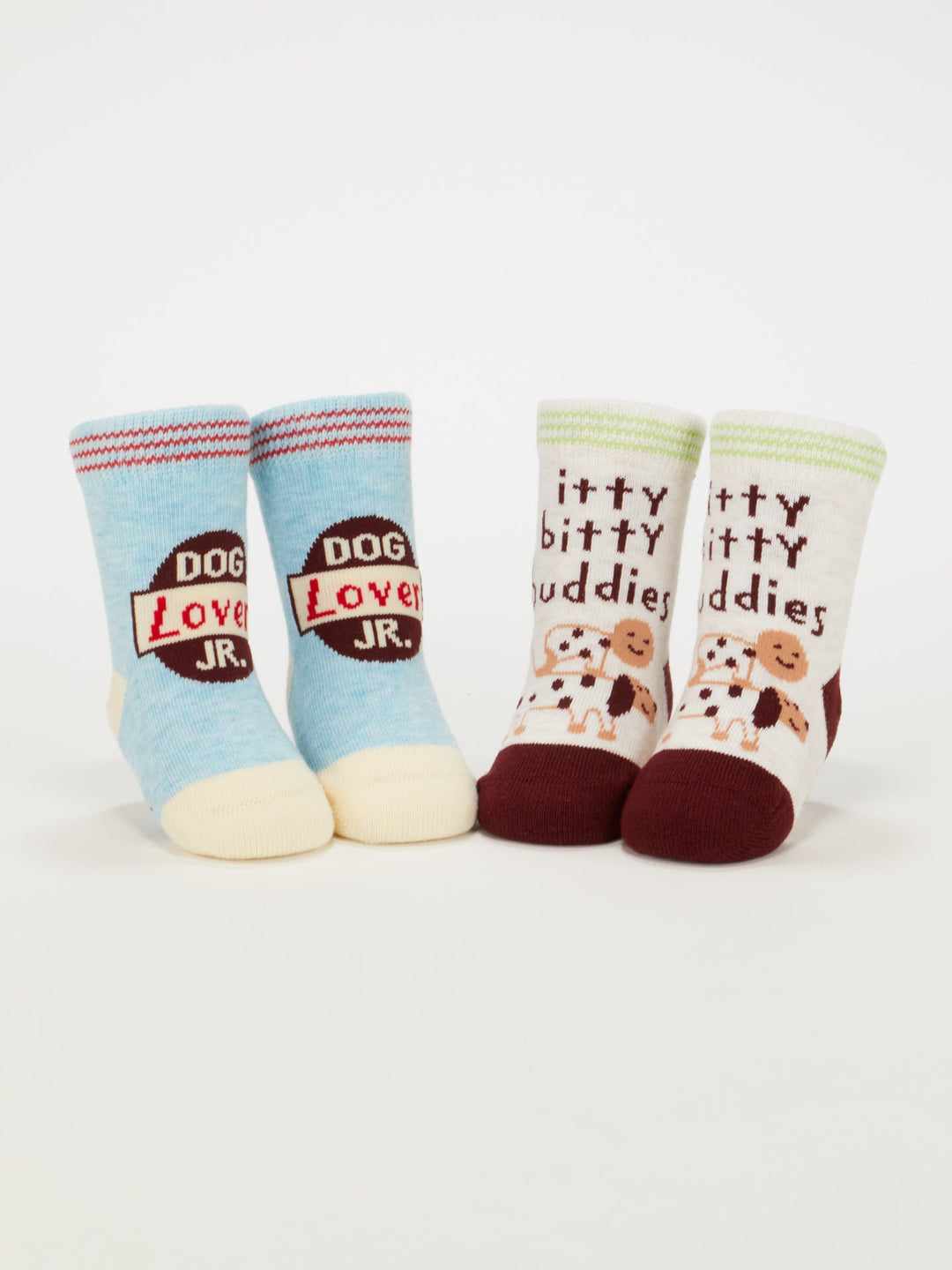 The Blue Q Dog Lover Jr./Itty Bitty Buddies Baby Socks set includes two pairs for ages 0–12 months: blue and cream with "DOG LOVER JR." text, and white and maroon with green cuffs, cartoon dogs, and "itty bitty buddies" wording.