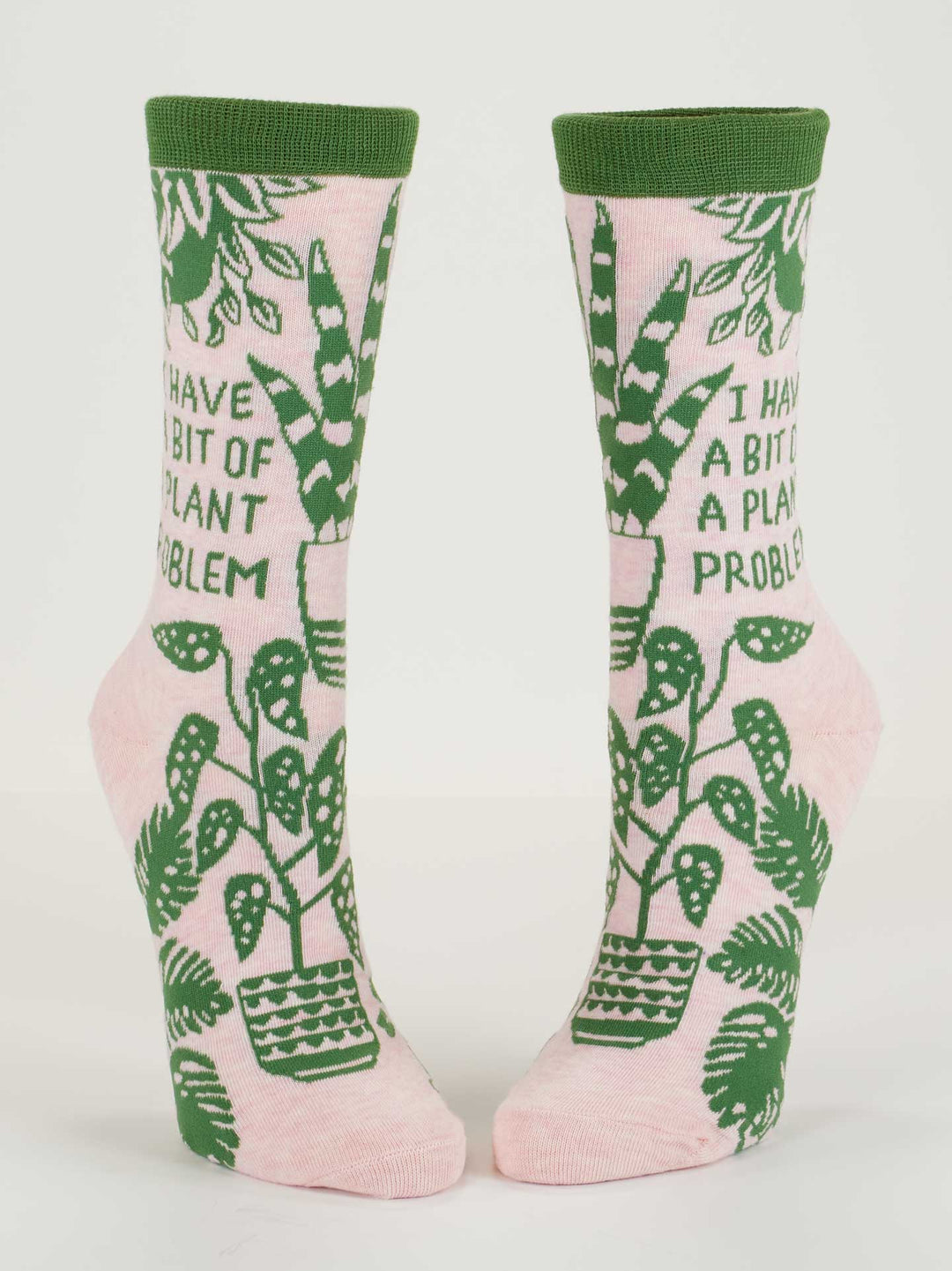 Blue Q’s I Have A Bit Of A Plant Problem W-Crew Socks are pink women’s socks with green trim, made from soft combed cotton. They feature the phrase "I HAVE A BIT OF A PLANT PROBLEM" plus monstera leaves and potted plants for a playful look.