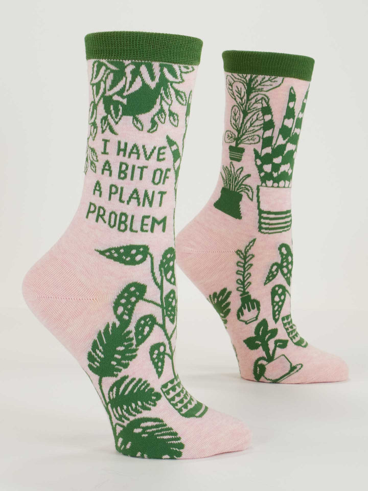 Blue Q’s “I Have A Bit Of A Plant Problem” W-Crew Socks feature pink combed cotton, green accents, potted plants (like monstera), and bold side text. Fits most women&