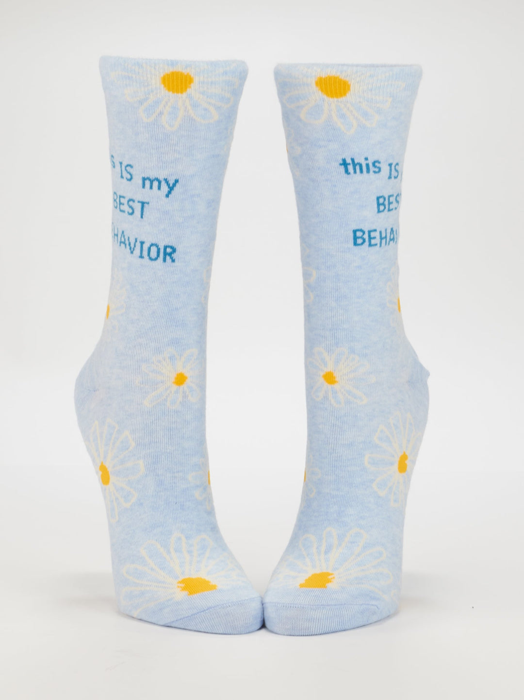 Blue Q’s This Is My Best Behavior W-Crew Socks feature light blue combed cotton, white and yellow daisies, and “this IS my BEST BEHAVIOR” in blue text. Fits women’s shoe size 5-10. Displayed upright on a white background.