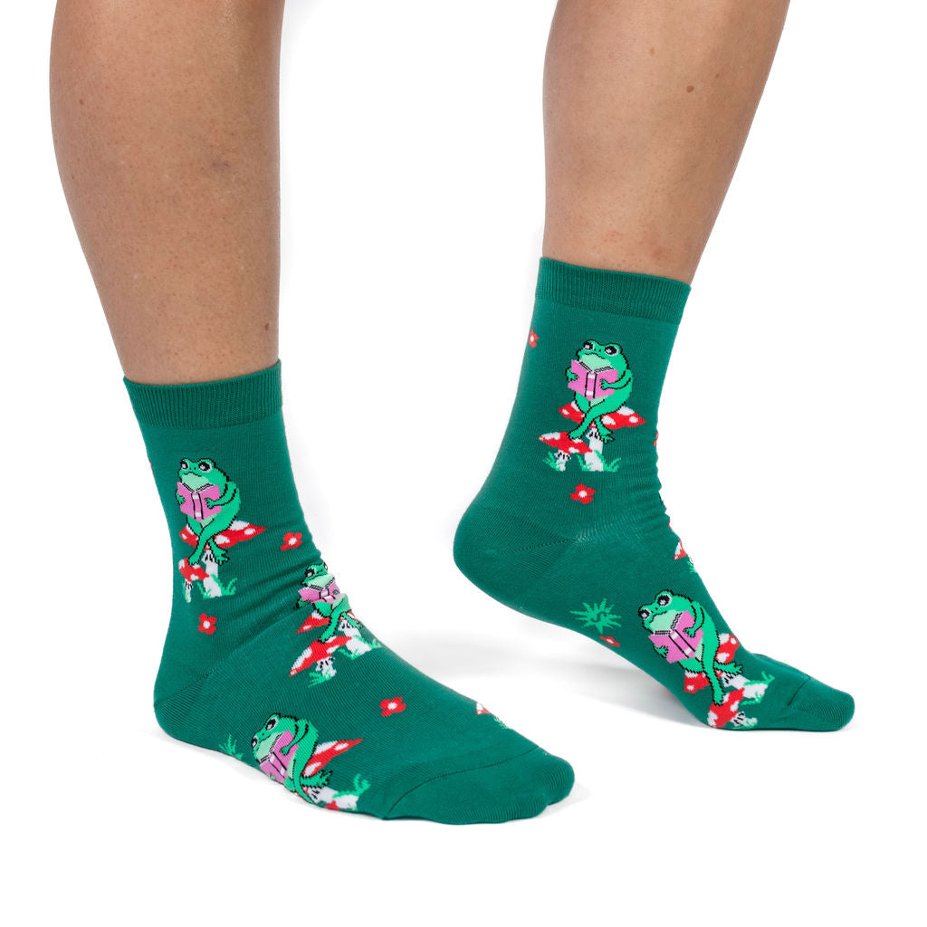 Toad Stool women's crew socks with a frog reading on a mushroom, model side view