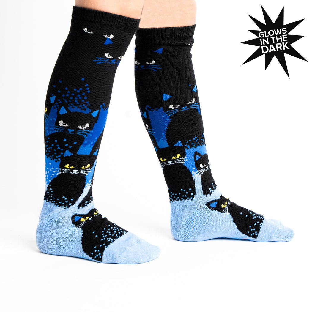 Kids' glow-in-the-dark cat knee high socks, worn front view showing black cats on legs