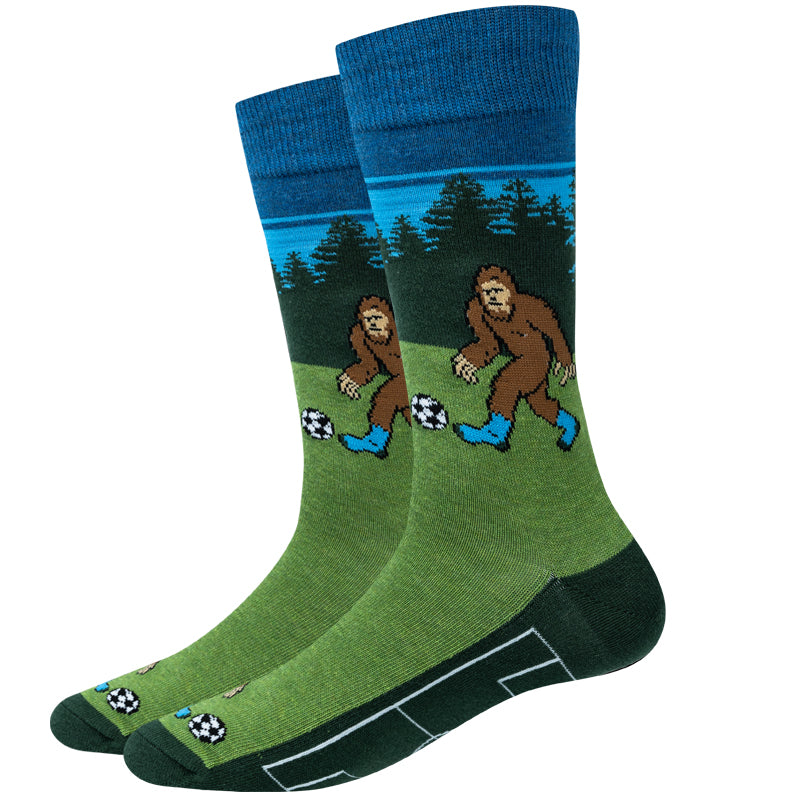 Unisex soccer Bigfoot crew socks in green with Bigfoot kicking a soccer ball by a pine forest, product shot of a pair