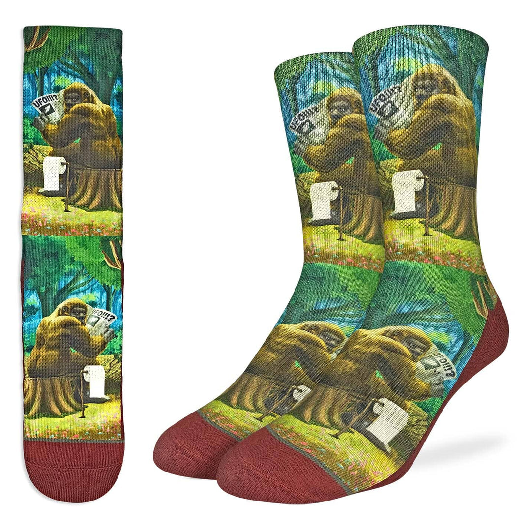 Men's crew socks with a painted forest scene of Bigfoot sitting on a stump reading a UFO newspaper with rust toes and heels