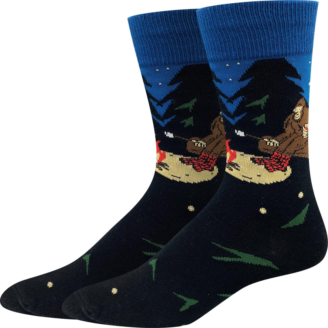 Pair of unisex crew socks showing Bigfoot roasting marshmallows by a campfire under a blue starry sky