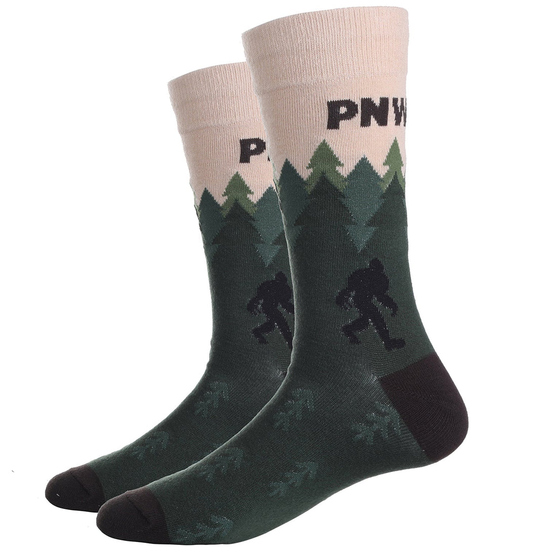 Pair of green PNW Bigfoot crew socks displayed flat, with a cream PNW cuff, evergreen treeline, and Sasquatch among the pines