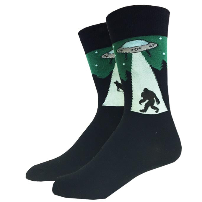 Black unisex crew socks showing a glowing UFO beaming up Bigfoot beneath a starry pine forest scene