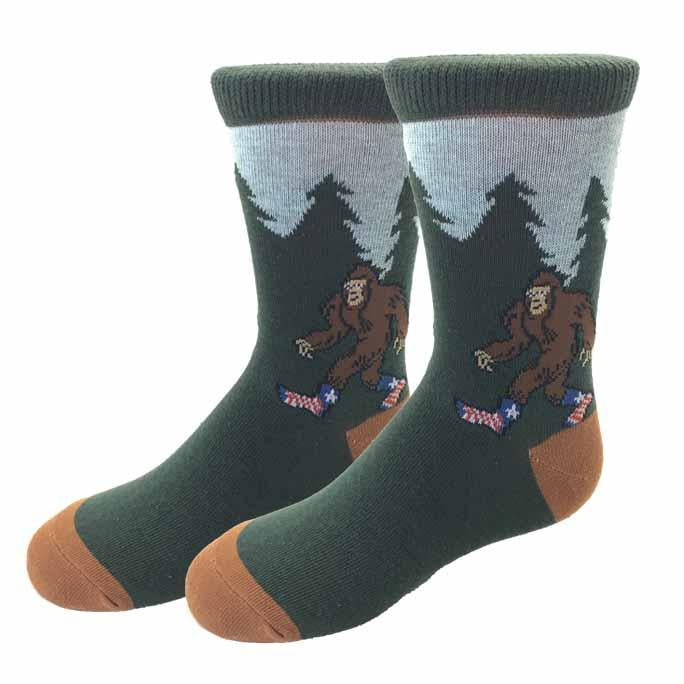 Kids' green crew socks with a cartoon Bigfoot in star-spangled shoes walking past pine trees, brown toe and heel