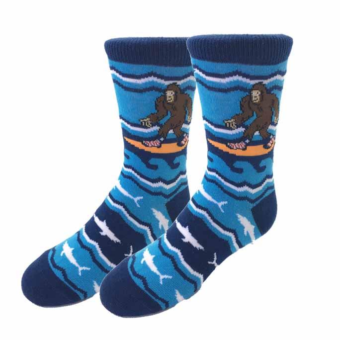 Kids' blue crew socks with a cartoon Bigfoot surfing on an orange board among waves and white fish