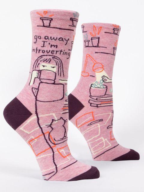 Side view of a women's pink crew sock with maroon heel and toe, illustrated with a homebody scene, a cat, and the text "go away I'm introverting"