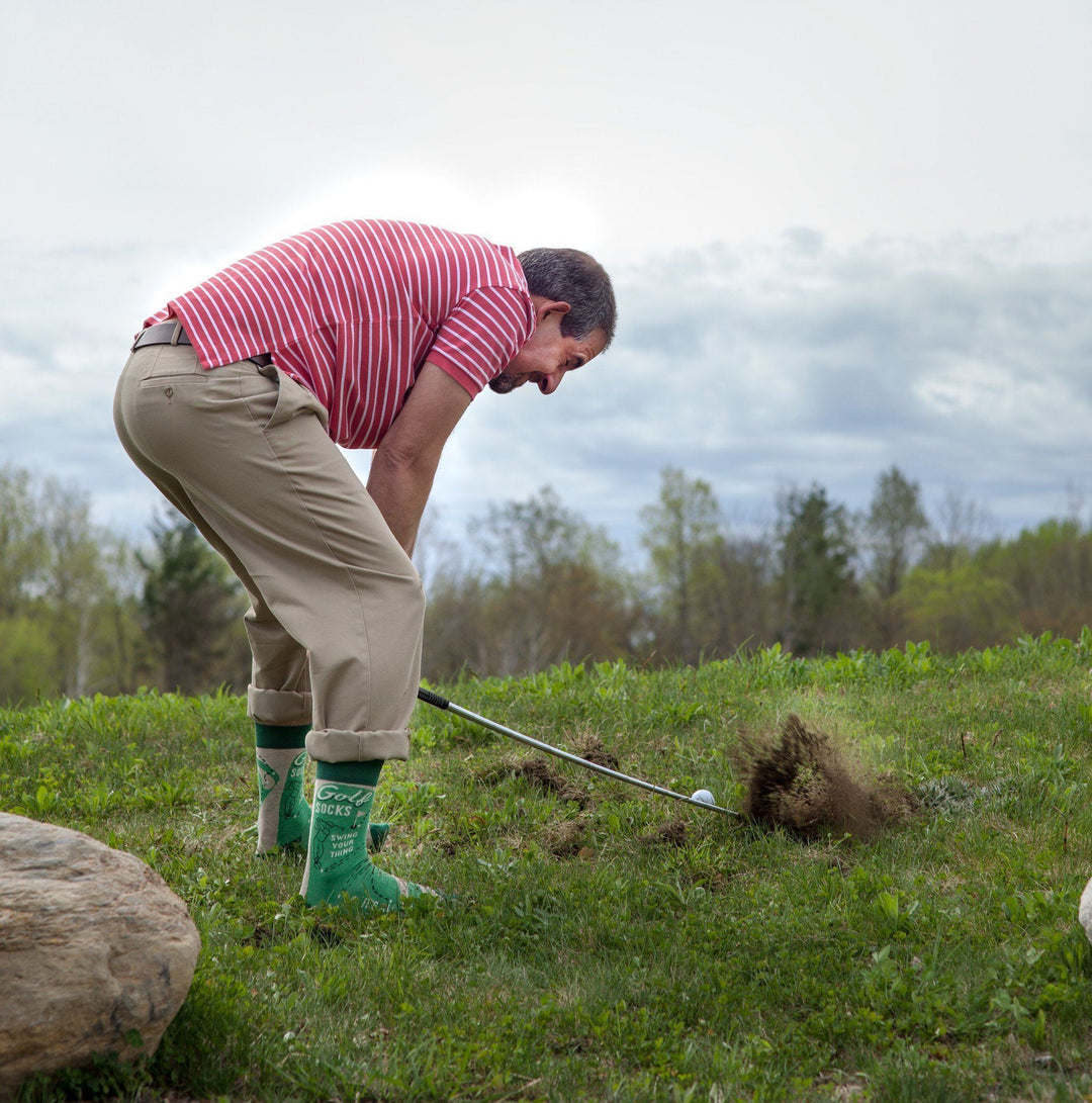 A golfer wearing green golf boots taking a swing in a field
