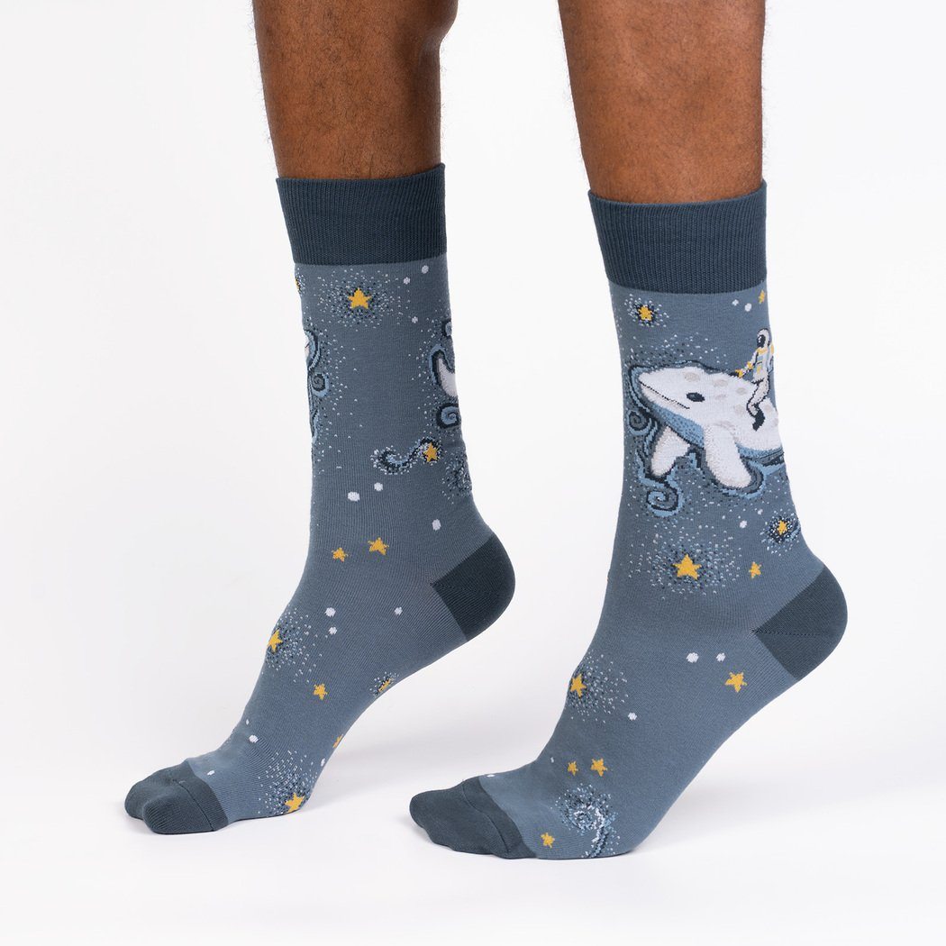 Person wearing slate-blue crew socks with an astronaut riding a beluga whale among stars, front view