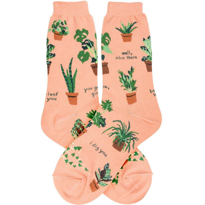 Pair of peach plant-themed crew socks laid flat with potted houseplants and puns like "well, aloe there" and "i dig you"