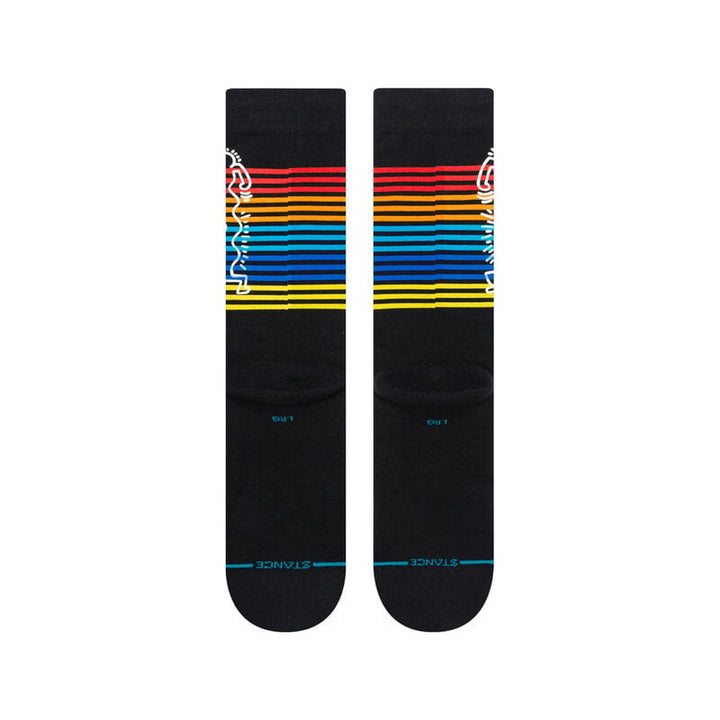 Angled view of black Keith Haring crew socks with rainbow stripes and the line-art figure