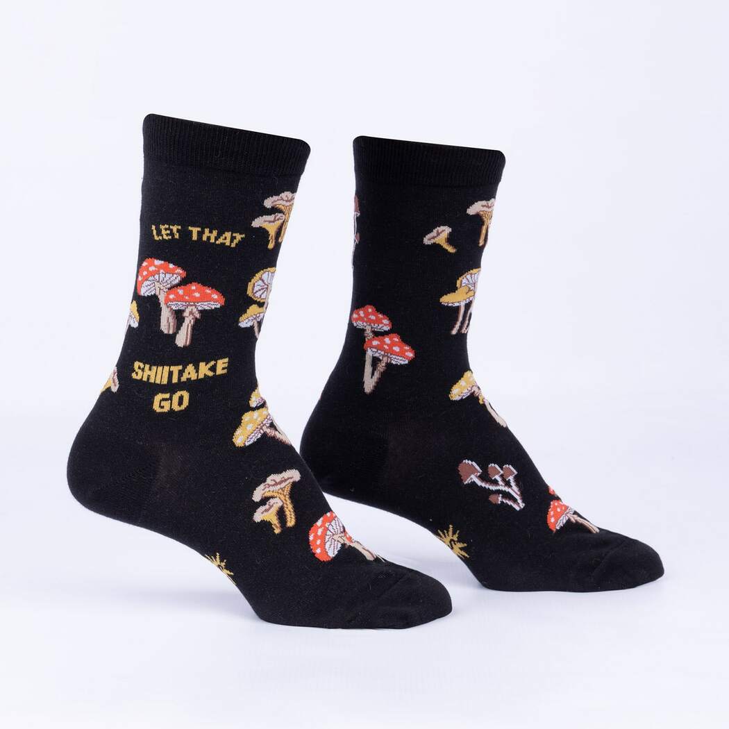 Flat-lay of black women's crew socks reading LET THAT SHIITAKE GO in gold among red and golden mushrooms