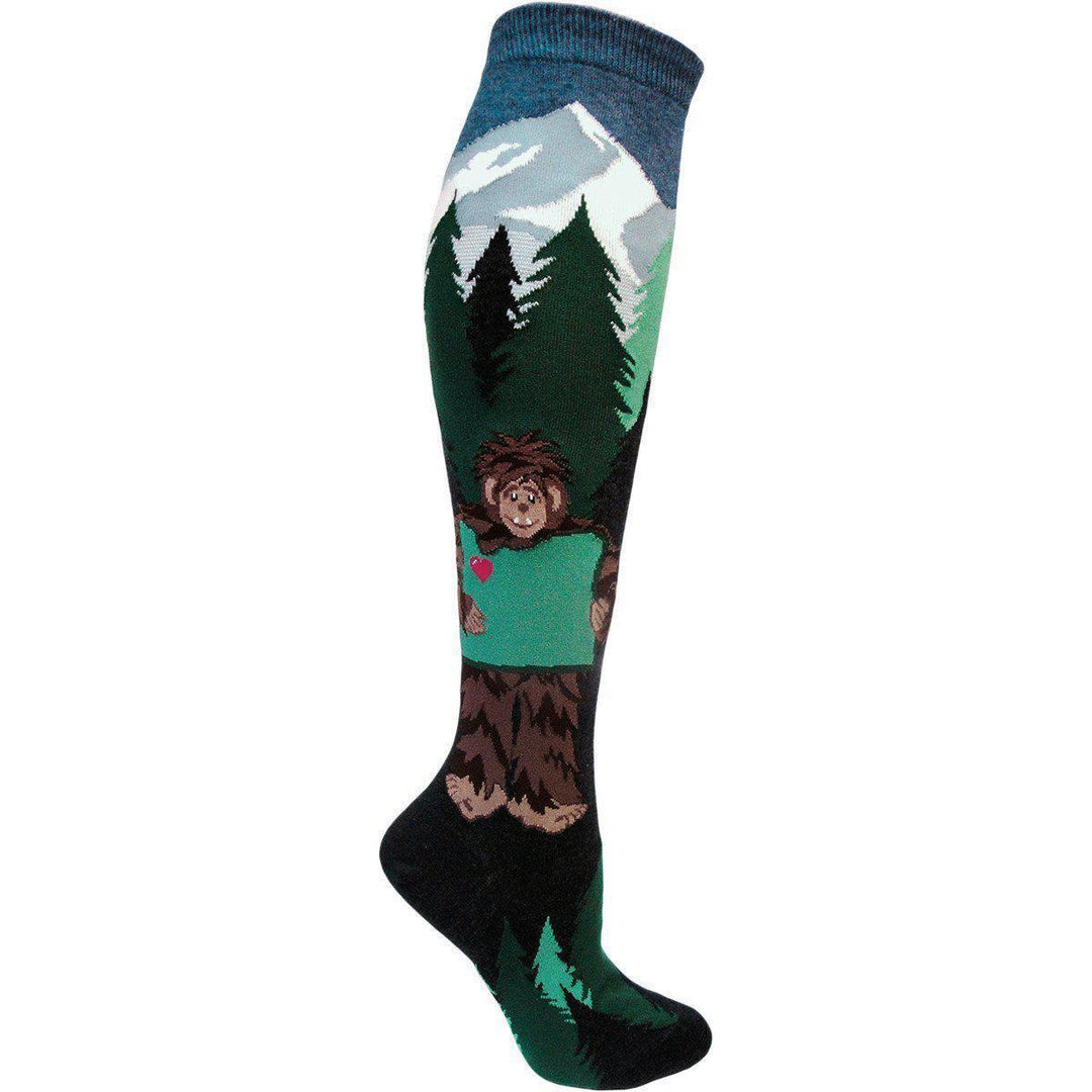 Single knee high sock showing a mountain, pine forest, and a brown Sasquatch holding a pink heart