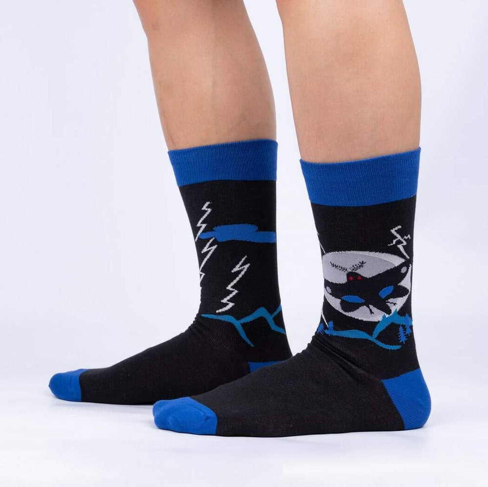 Side view of the Mothman crew socks worn on legs, showing the cryptid, moon, and blue mountain ridge
