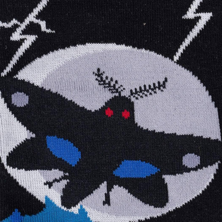 Close-up knit detail of the winged Mothman with glowing red eyes against the grey moon