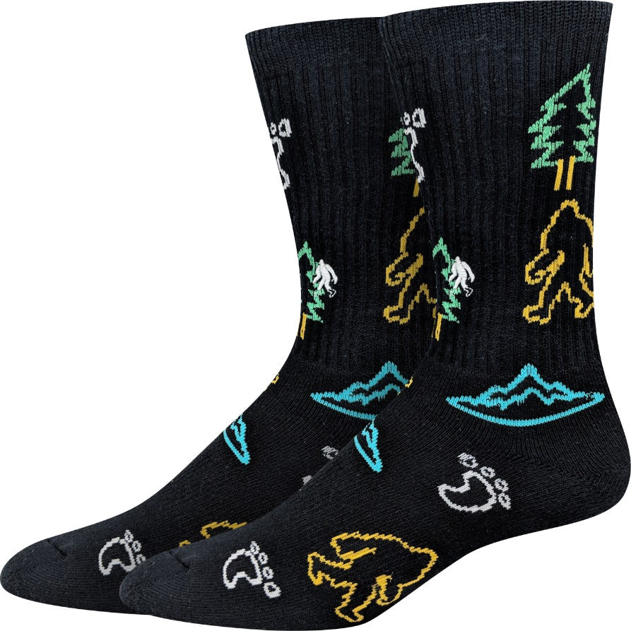 Men's black active crew socks with neon Sasquatch figures, pine trees, mountains, and paw prints in yellow and teal