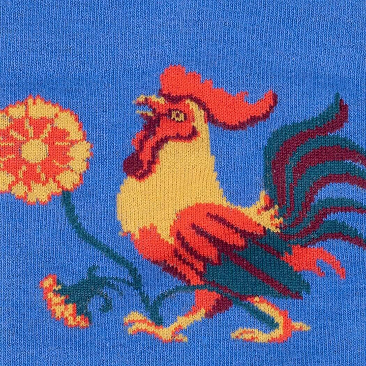 Close-up knit detail of a single red and gold crowing rooster beside an orange marigold bloom