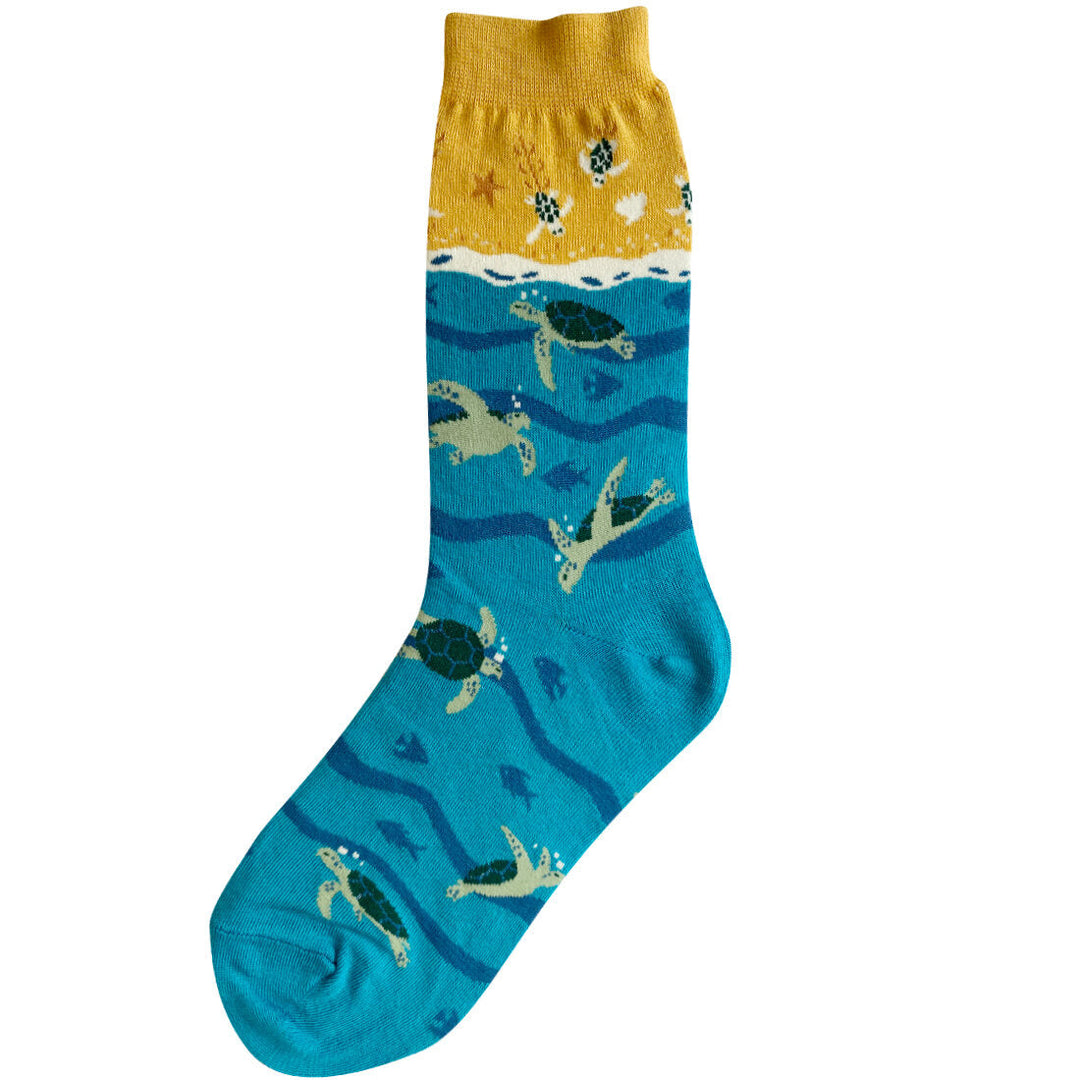 Women's crew sock with golden sandy beach and shells at the cuff fading into teal ocean waves where green sea turtles swim among fish