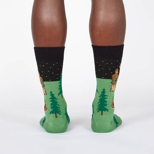 Back view of the green Bigfoot camping socks worn, showing evergreens and Sasquatch figures down the leg