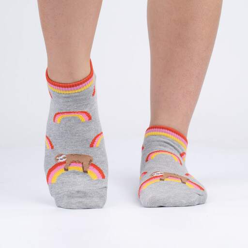 Women's grey sloth ankle socks shown on feet, side angle, with rainbows and a lounging sloth, orange and pink striped cuff