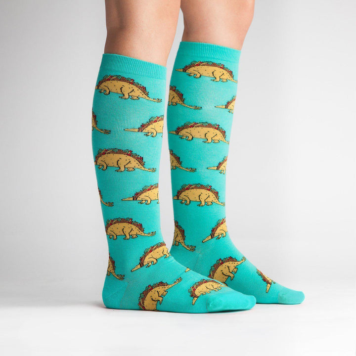 Model wearing turquoise taco dinosaur knee high socks, side view