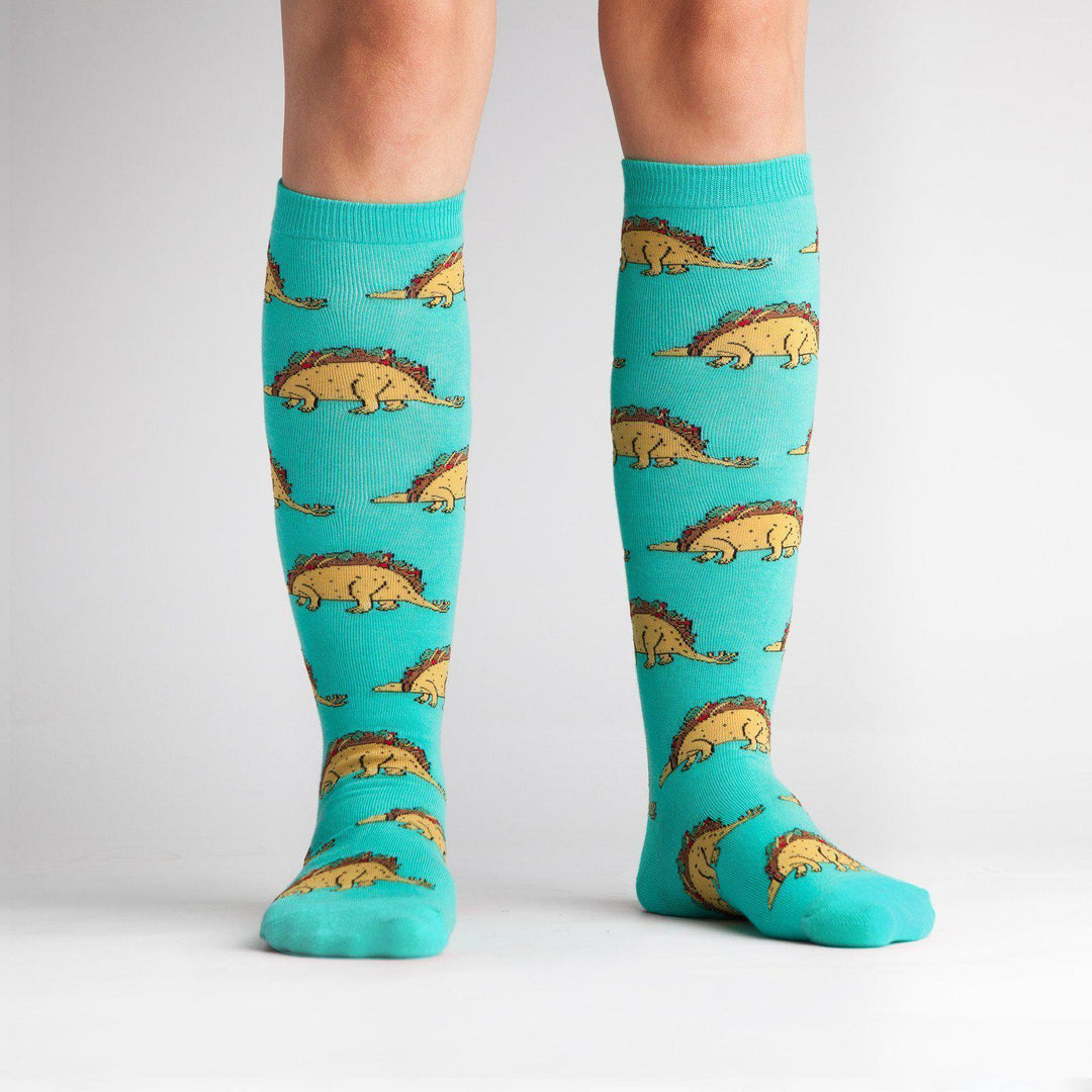 Model wearing turquoise taco dinosaur knee high socks, front view