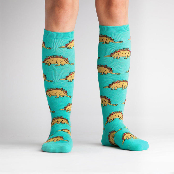 Model wearing turquoise taco dinosaur knee high socks, front view