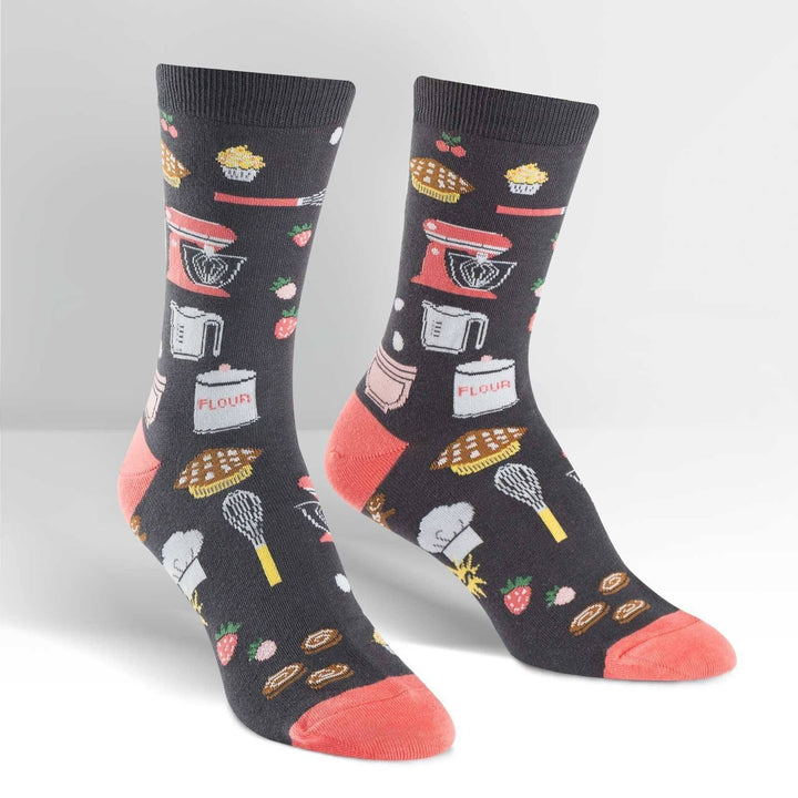 Pair of charcoal gray crew socks covered in baking icons like a stand mixer, whisks and pies, coral heel and toe