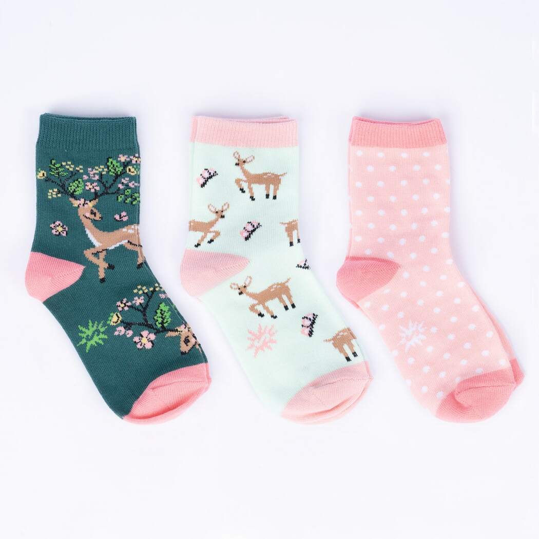 Flat-lay of three kids' crew socks: a green pair with a blossom-antlered deer, a mint pair with fawns and flowers, and a pink polka-dot pair
