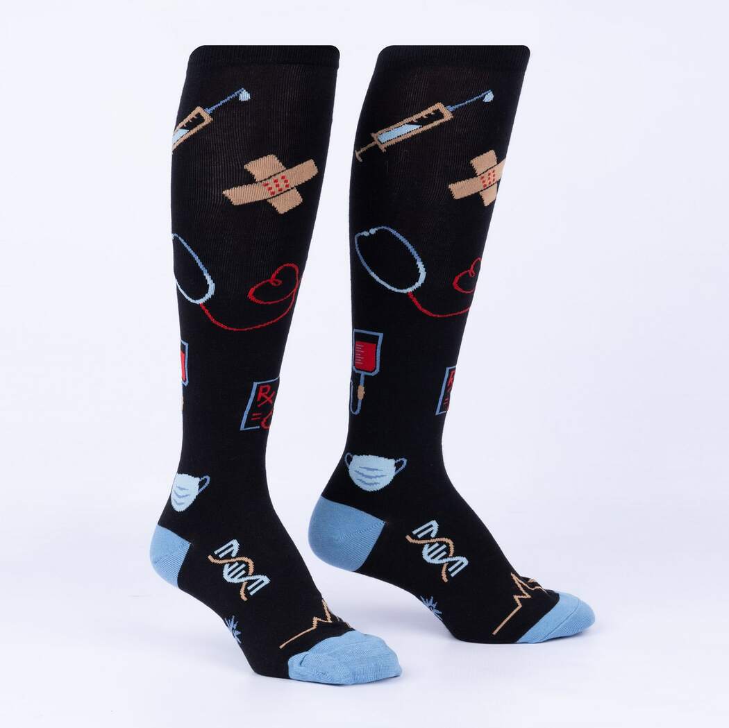 Flat-lay of black women's medical knee high socks with syringes, bandages, stethoscopes, blood bags, and DNA in blue and red, with blue heels